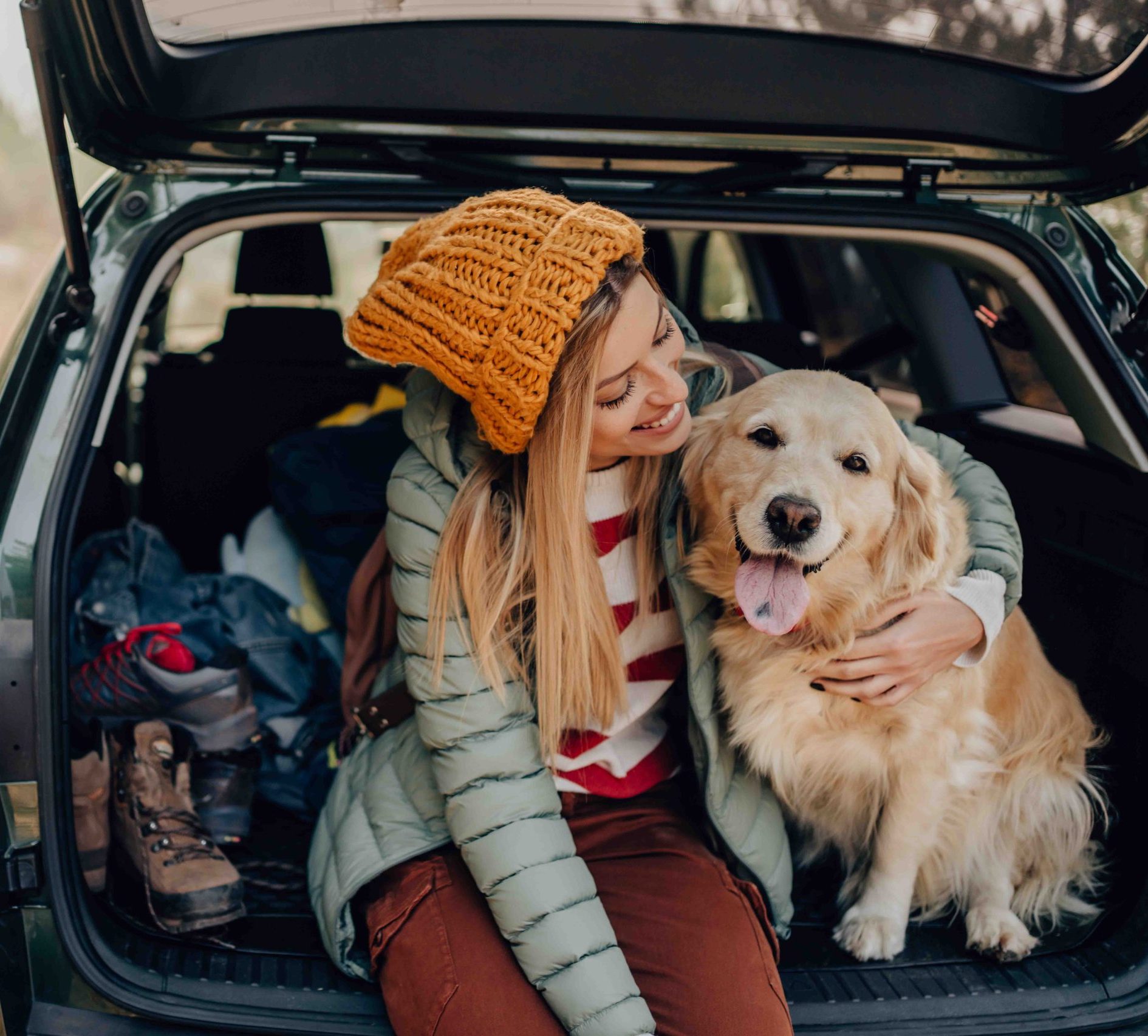 young smiling woman and her dog sitting the trunk of a car